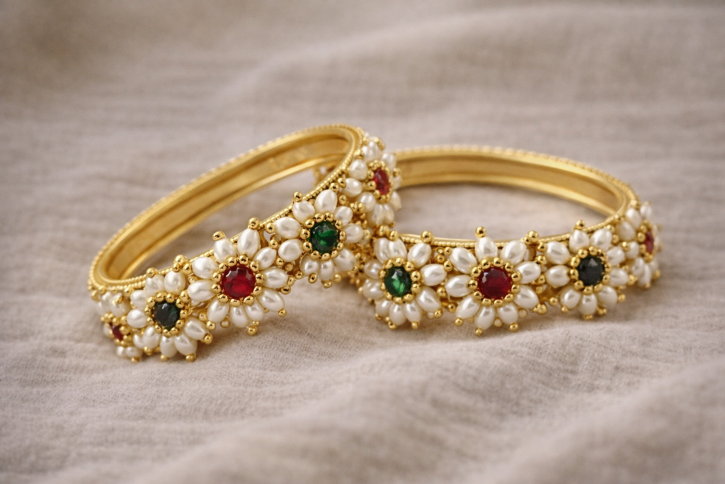 “Handcrafted pearl floral bangles with red and green stones in gold-toned detailing”