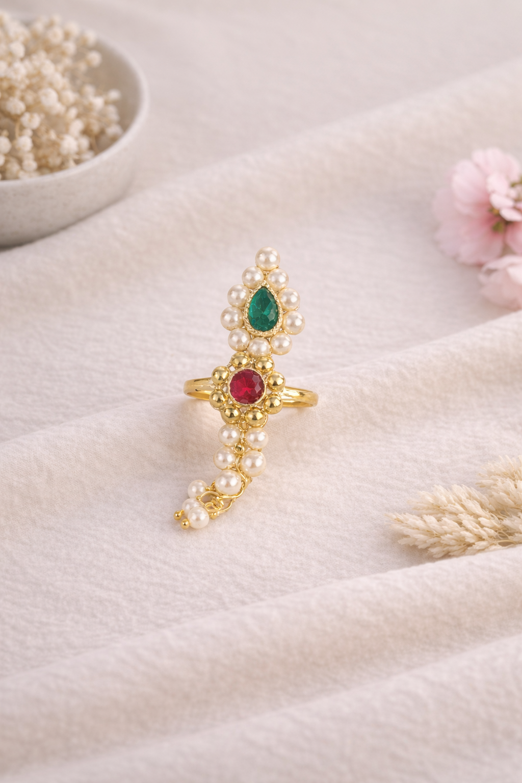 Pearl Nath finger ring with red and green stones and pearl detailing on a soft cream fabric background