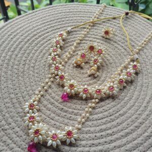 Parijatak Saaj pink pearl necklace set with floral motifs, kundan-style pink stones, layered pearl strands, and matching jhumka earrings on white background