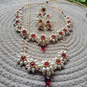 Parijatak Saaj red pearl necklace set with floral kundan motifs and matching jhumka earrings on white background