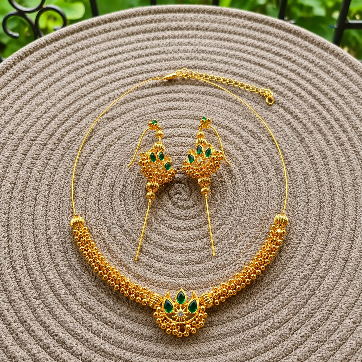 Chandra Invisible Choker & Ear Cuffs in green displayed on a woven mat with a blurred garden background.