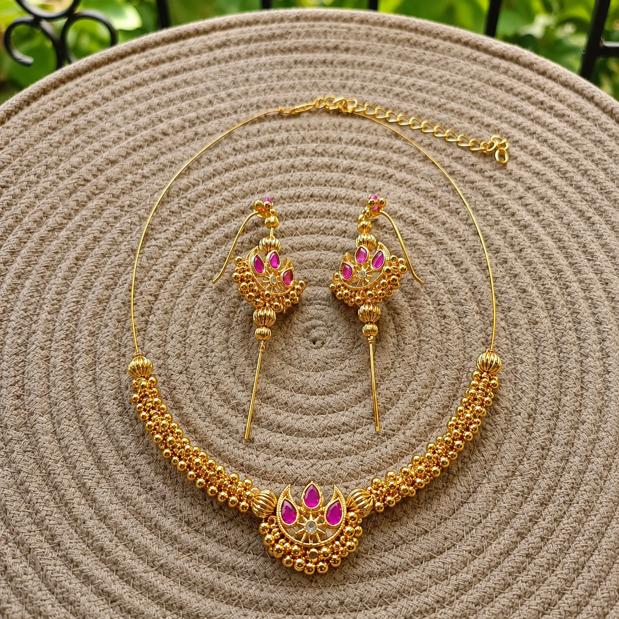 Chandra Invisible Choker & Ear Cuffs in pink displayed on a woven mat with a blurred garden background.