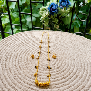 Golden Mangalsutra with matching earrings displayed on a woven mat with a blurred garden background.