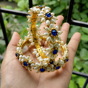 Parijatak Bangles – Blue Parijatak Bangles - Blue held in a hand, showing white floral beads and blue centre stones.